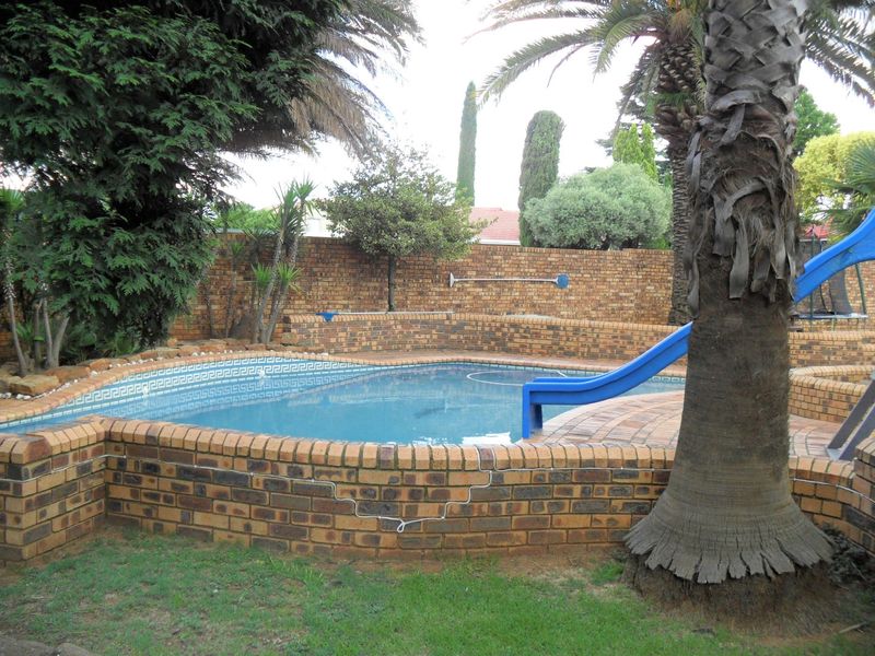 Outdoor swimming pool area featuring a brick-surrounded pool with an integrated slide and established garden landscaping.