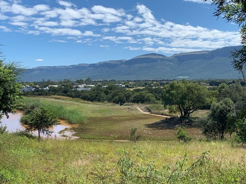A scenic view of the surrounding landscape featuring natural vegetation, a water body, and a distant mountain range.