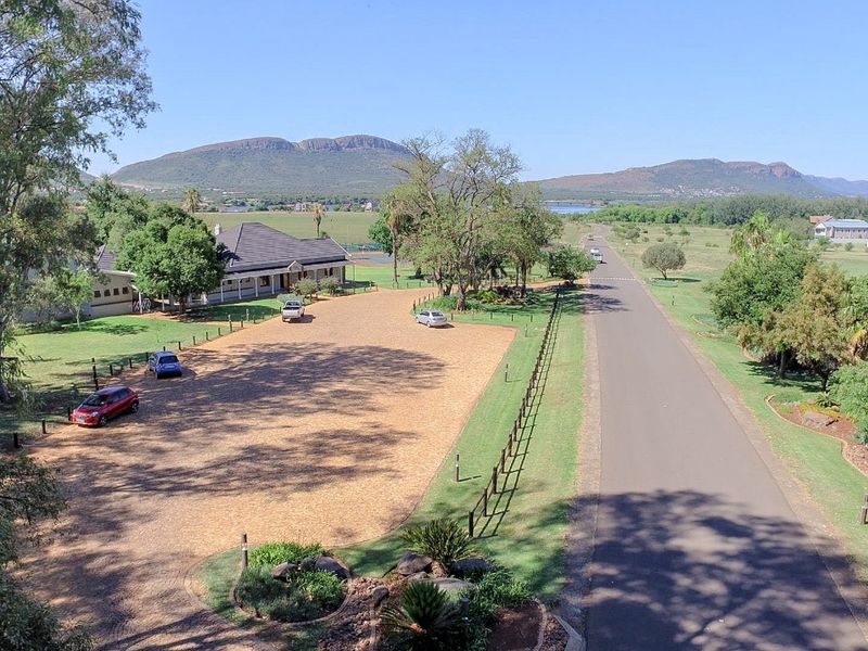 An aerial view of a residential property featuring a large paved driveway, established landscaping, and scenic mountain views in the background.