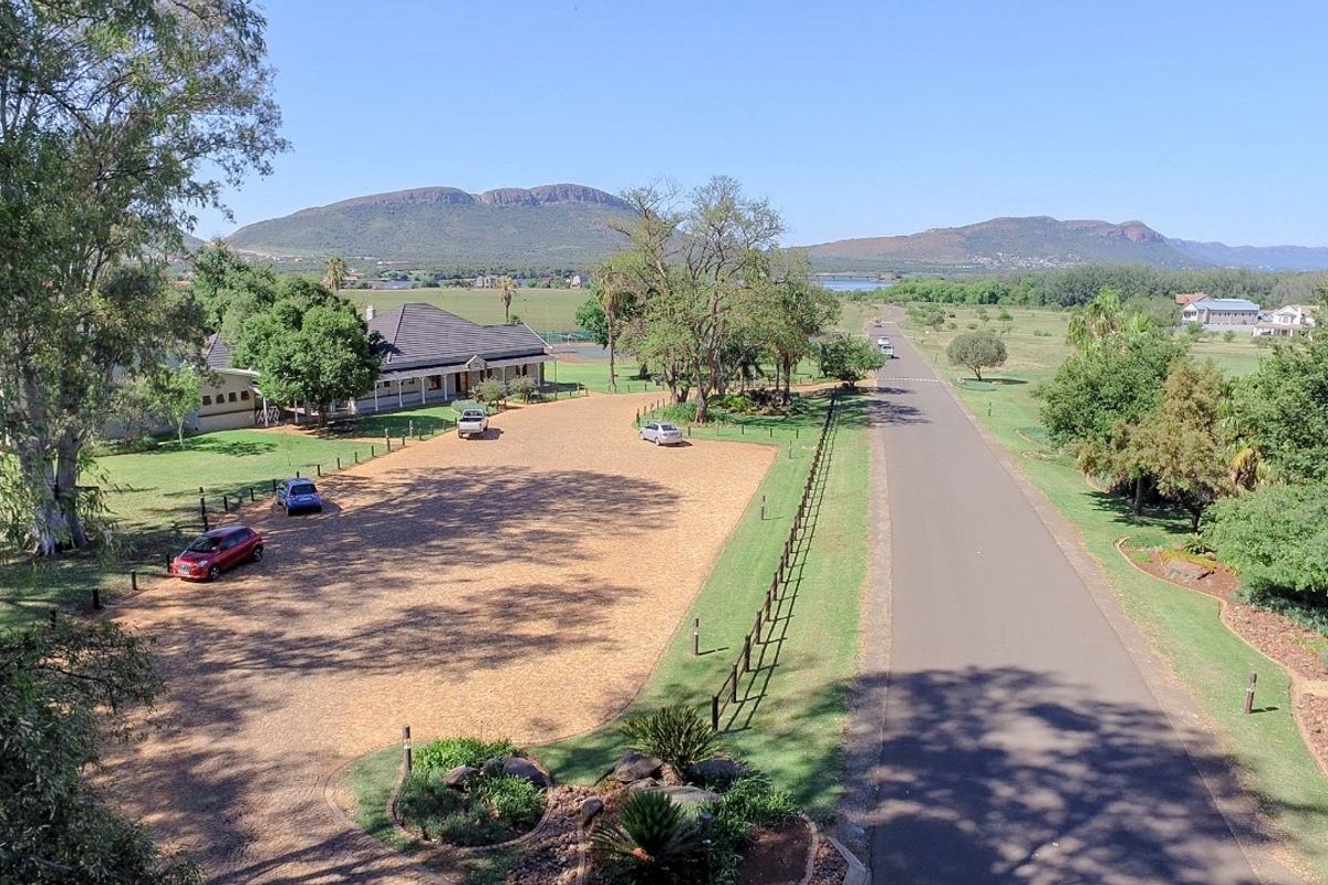 An aerial view of a residential property featuring a large paved driveway, established landscaping, and scenic mountain views in the background.