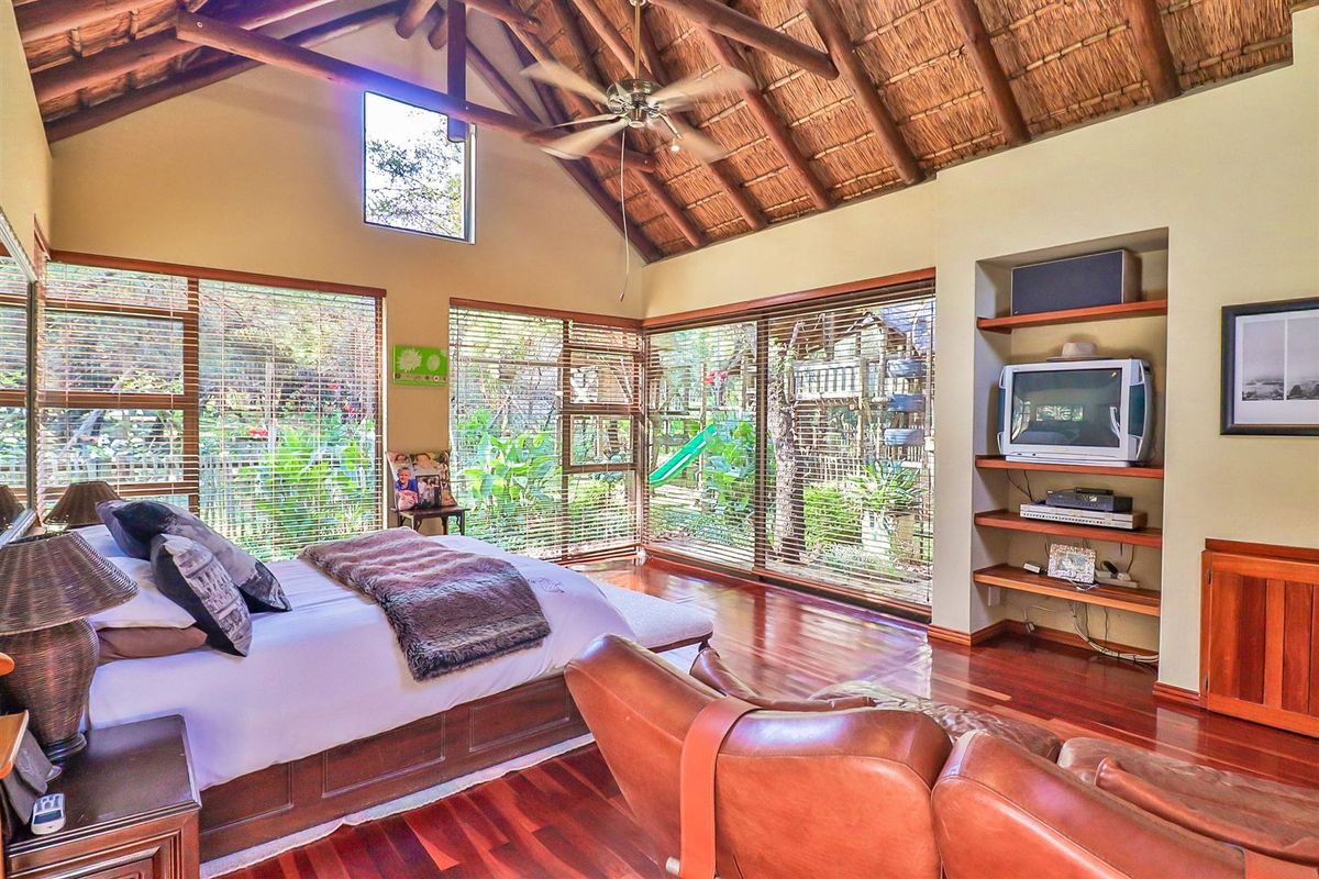 Spacious bedroom featuring a vaulted thatched ceiling with exposed timber rafters, hardwood flooring, and large windows overlooking the garden.