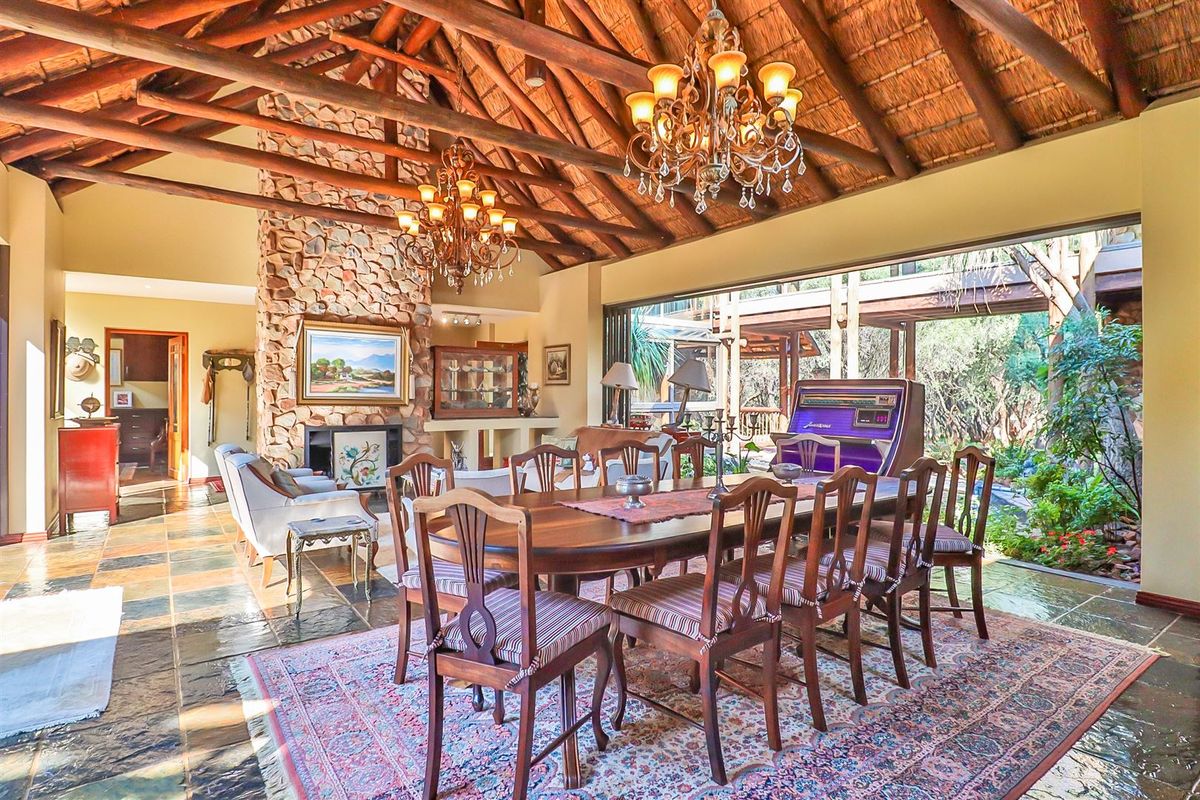 Spacious living and dining area featuring a high thatched ceiling with exposed timber rafters, a prominent stone fireplace, and large sliding doors to the garden.