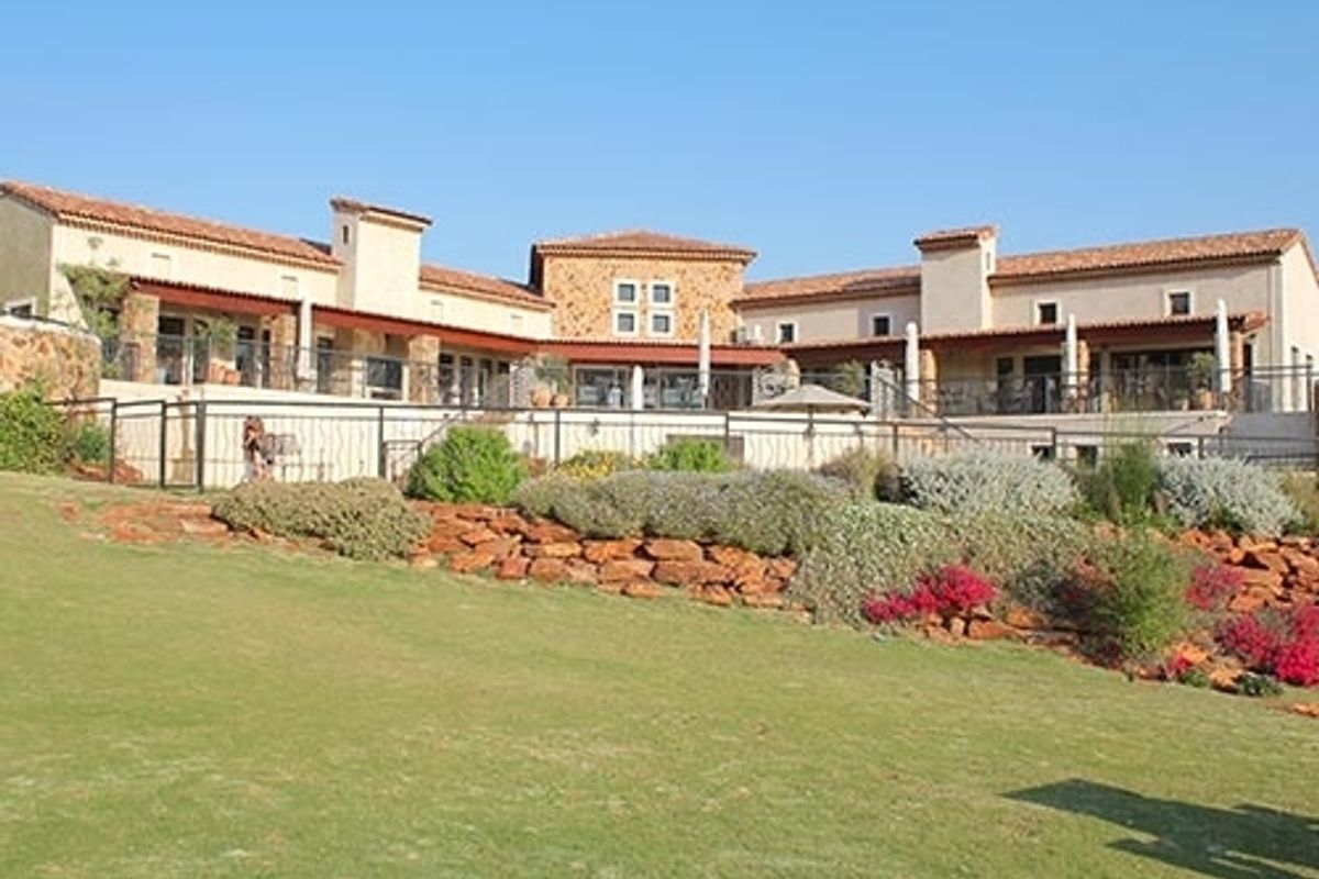 A spacious rear view of a Mediterranean-style residence featuring stone accents, terracotta roof tiles, and a well-maintained garden with a retaining wall.