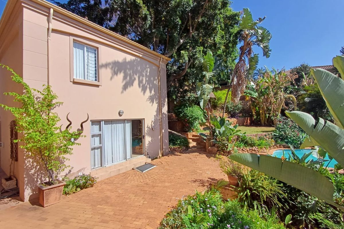 Rear exterior view featuring a brick paved patio, landscaped garden with mature trees, and a swimming pool area.