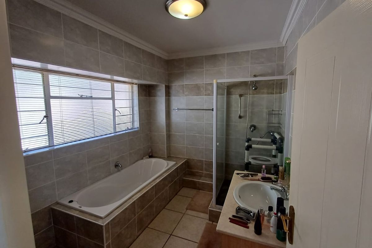 A functional bathroom featuring a built-in bathtub, a separate glass-enclosed shower, and a vanity basin with tiled finishes throughout.