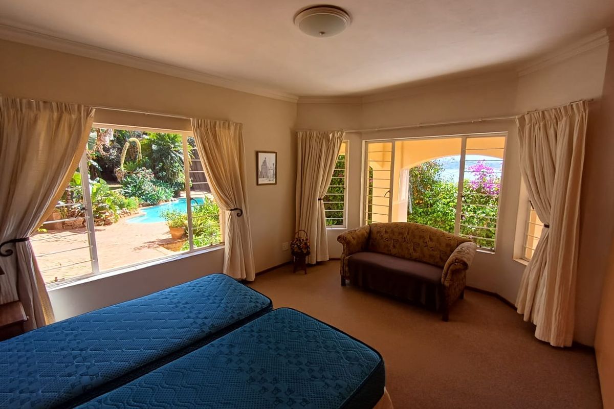 Spacious bedroom featuring large windows with garden and pool views, carpeted flooring, and ample natural light.