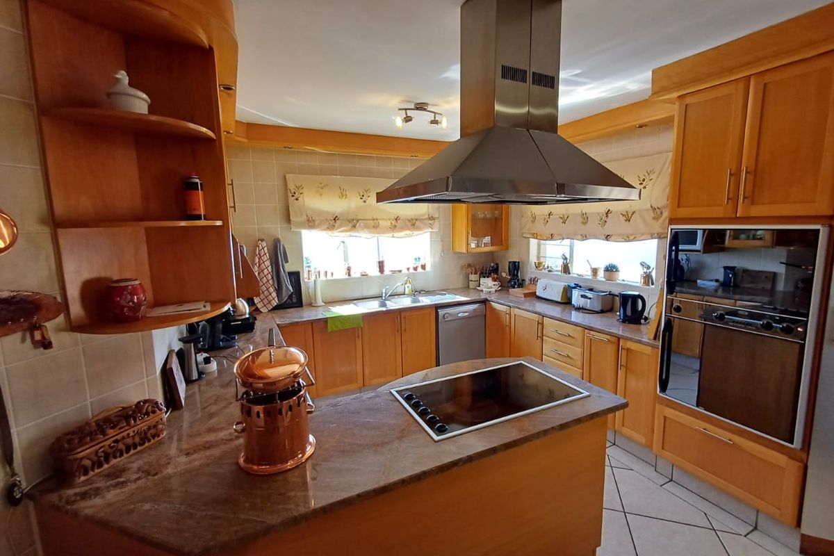 A functional kitchen featuring wooden cabinetry, stone countertops, a central island with a built-in hob, and stainless steel appliances.