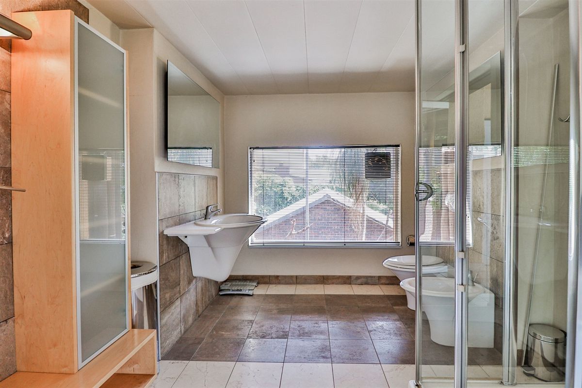 A functional bathroom featuring a wall-mounted basin, glass shower enclosure, bidet, and toilet with neutral tiled finishes and built-in storage cabinetry.