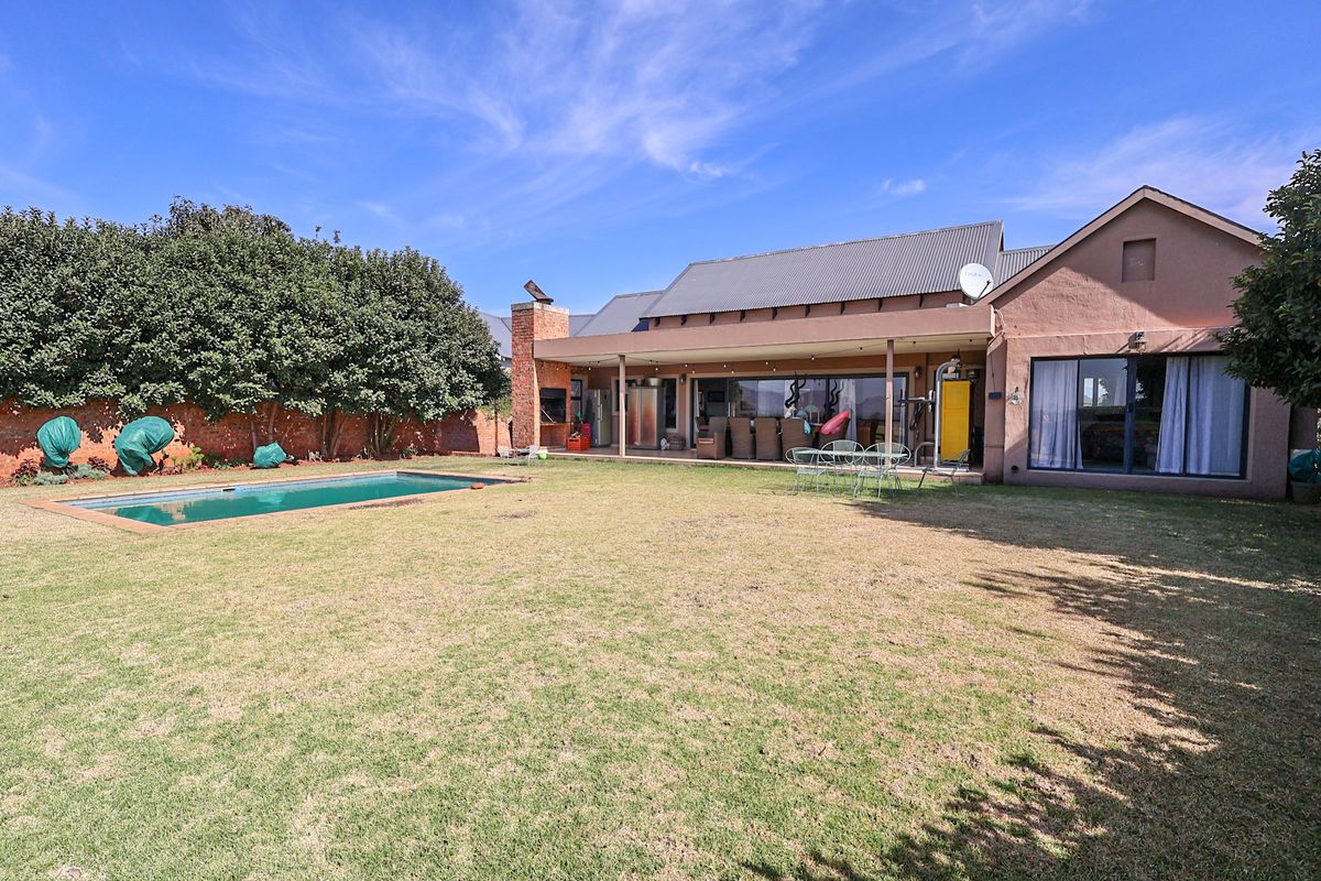 Spacious rear garden featuring a swimming pool, a covered patio with a built-in fireplace, and direct access to the home via sliding glass doors.