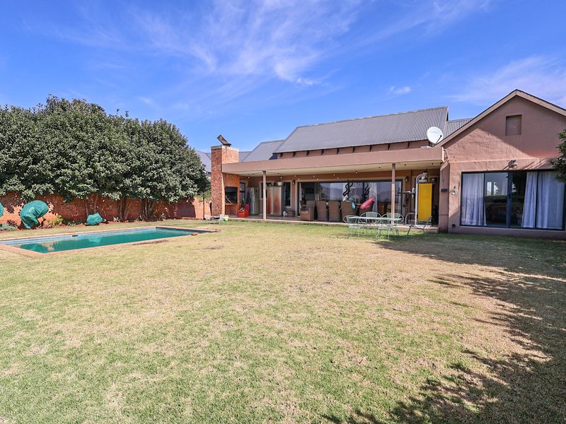Spacious rear garden featuring a swimming pool, a covered patio with a built-in fireplace, and direct access to the home via sliding glass doors.