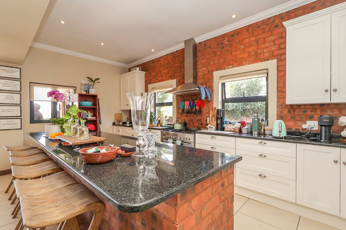 A well-appointed kitchen featuring a large granite-topped island, exposed brick feature wall, shaker-style cabinetry, and integrated stainless steel appliances.