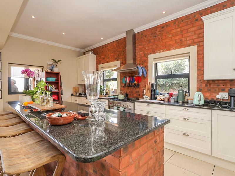 A well-appointed kitchen featuring a large granite-topped island, exposed brick feature wall, shaker-style cabinetry, and integrated stainless steel appliances.