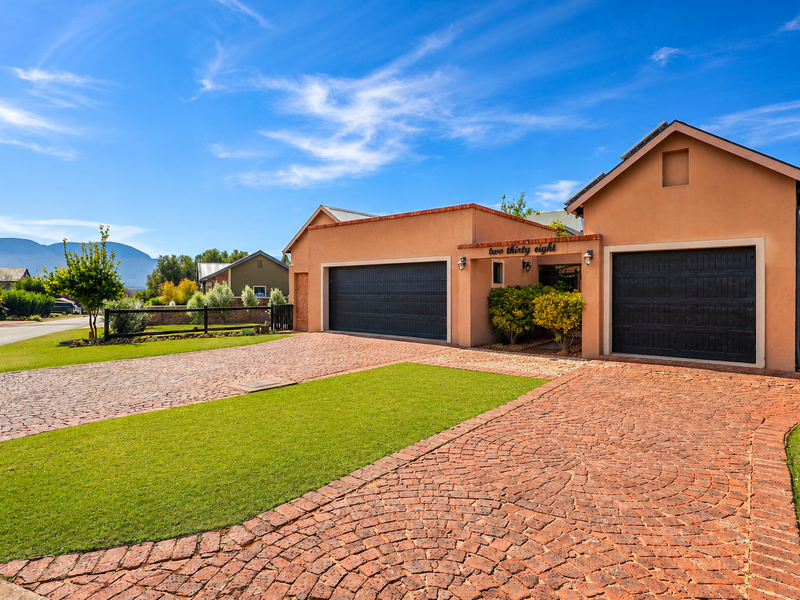 Front elevation of a well-maintained house featuring a paved driveway, double and single garages, and solar panels under a clear blue sky.