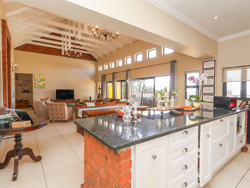 Spacious open-plan living area featuring a kitchen with granite island, exposed brick accents, and high vaulted ceilings with exposed timber trusses.