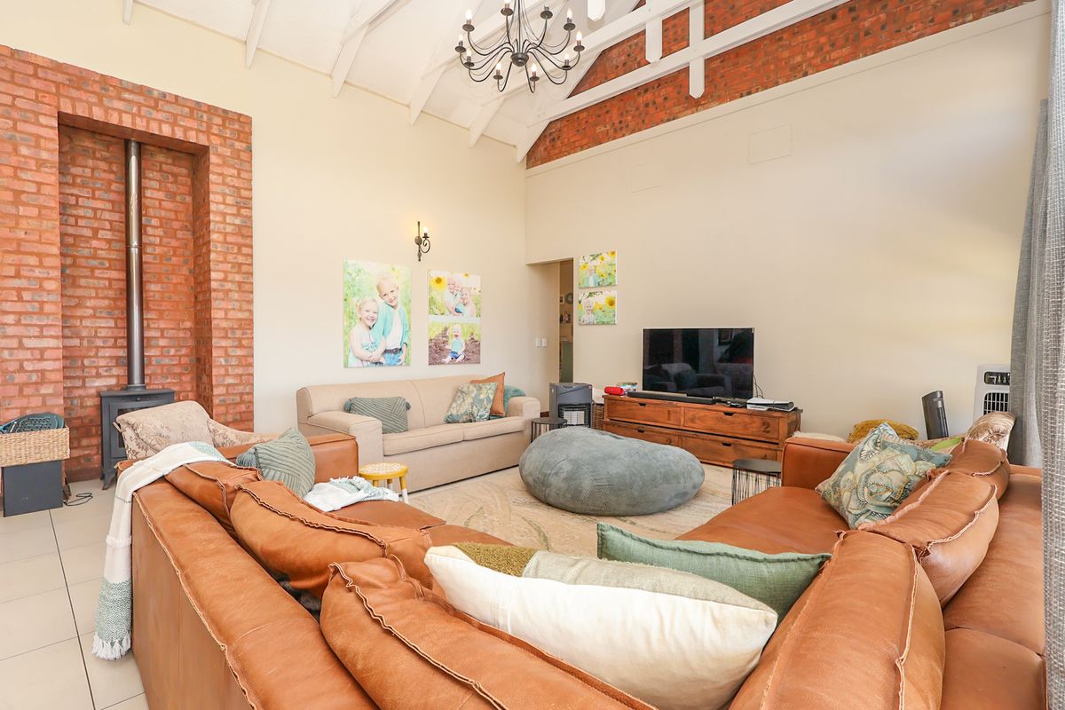 Spacious living room featuring a high vaulted ceiling with exposed timber trusses, a striking exposed brick feature wall, and a freestanding wood-burning fireplace.