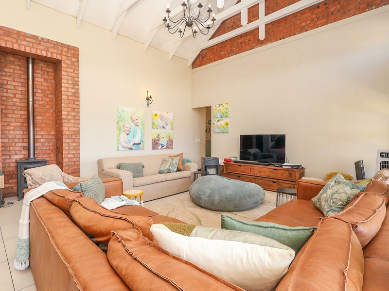 Spacious living room featuring a high vaulted ceiling with exposed timber trusses, a striking exposed brick feature wall, and a freestanding wood-burning fireplace.