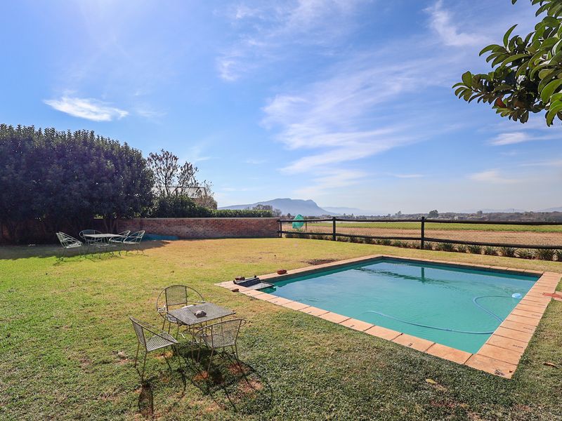 A spacious backyard featuring a swimming pool, manicured lawn, and scenic mountain views, enclosed by a brick wall and post-and-rail fencing.