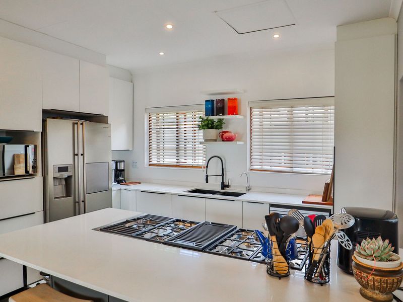 Modern kitchen featuring sleek white cabinetry, quartz countertops, a central island with a built-in gas hob, and high-quality finishes throughout.