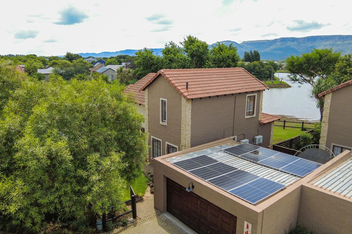 Aerial view of a townhouse featuring a tiled roof, solar panel installation, and a paved driveway, set within a scenic estate near the water.