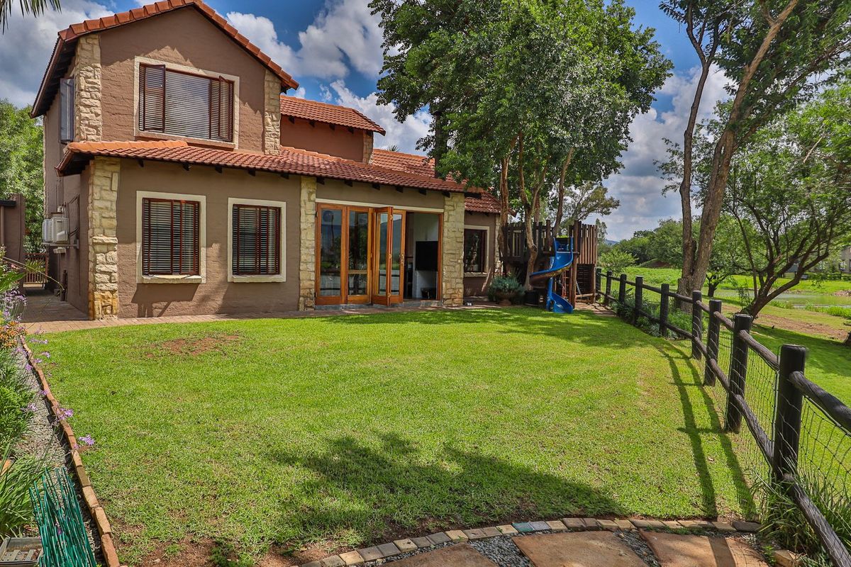 Rear view of a townhouse featuring a well-maintained lawn, stone-clad exterior walls, terracotta roof tiles, and a timber fence overlooking the surrounding landscape.