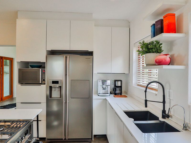 Modern kitchen featuring white cabinetry, sleek countertops, a double sink with a gooseneck faucet, and a gas cooktop, offering a clean and functional workspace.