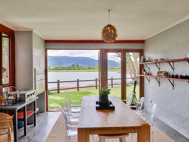 A bright, covered patio area featuring a built-in braai, timber-framed folding doors, and expansive views of the lake and mountains.