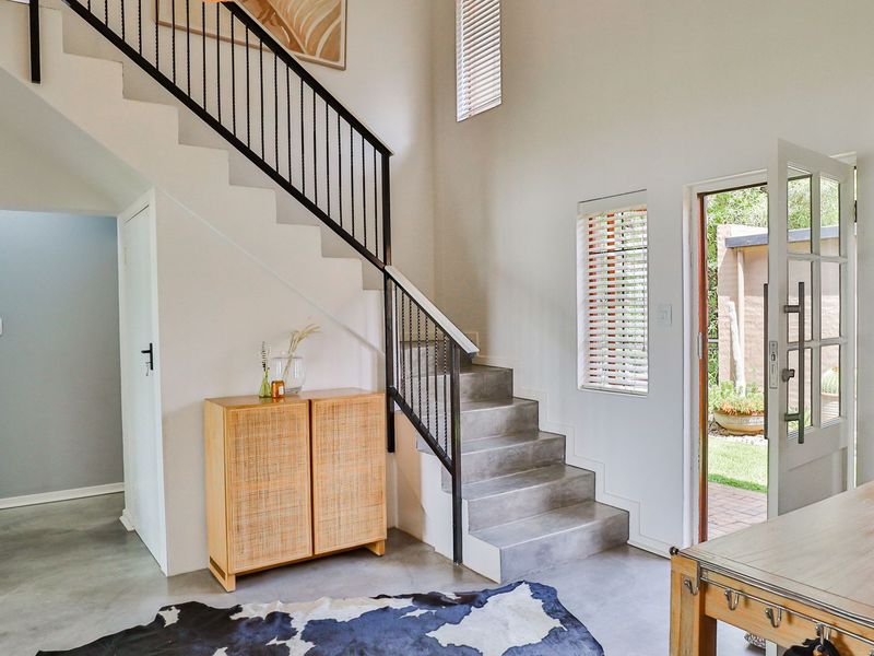 Bright entrance hall featuring a modern staircase with metal balustrade, polished concrete flooring, and direct access to the garden through a glass-paneled door.