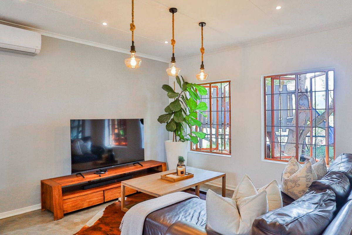 A well-lit living room featuring concrete flooring, recessed downlights, a wall-mounted air conditioner, and timber-framed windows with security bars.