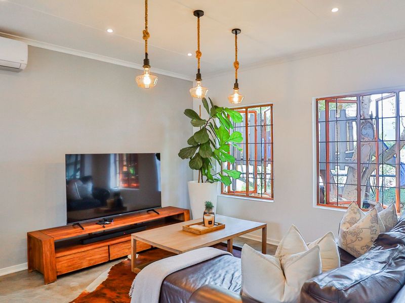 A well-lit living room featuring concrete flooring, recessed downlights, a wall-mounted air conditioner, and timber-framed windows with security bars.