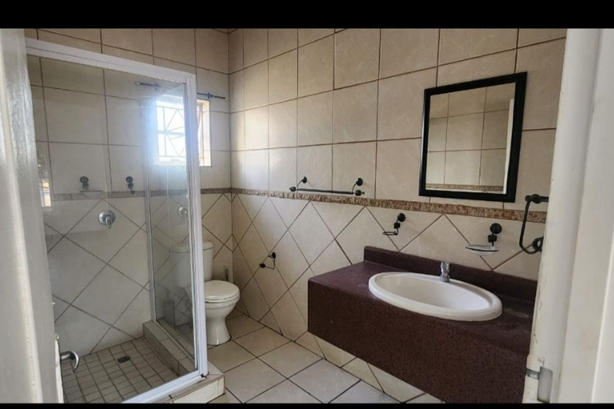 A functional bathroom featuring a glass-enclosed shower, a wall-mounted vanity with a basin, and neutral wall and floor tiling.