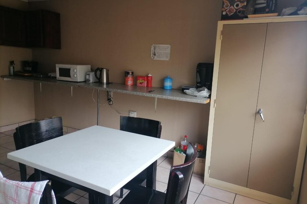 A functional kitchenette area featuring a laminate countertop, wall-mounted cabinetry, and tiled flooring, suitable for a breakroom or utility space.