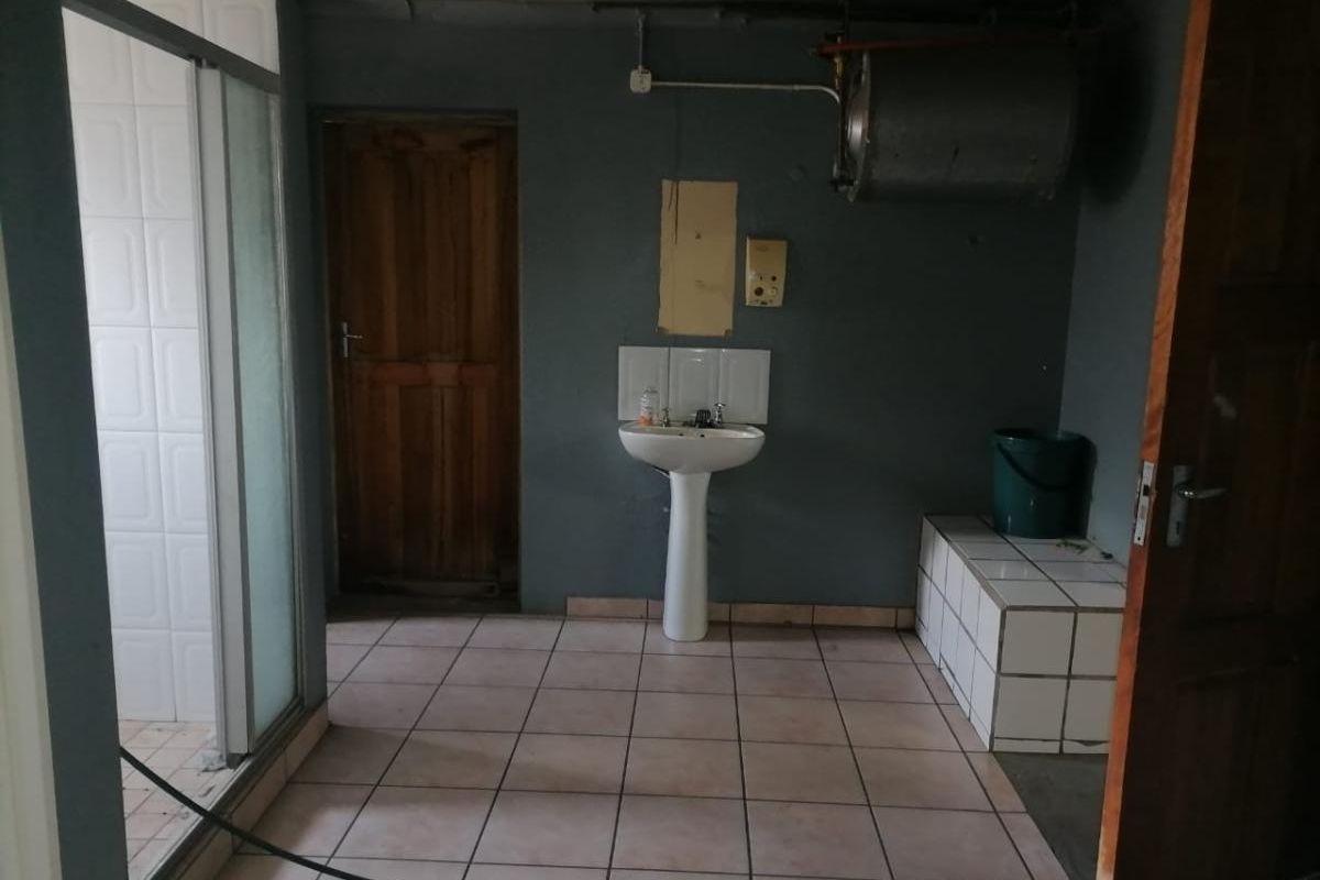 A functional bathroom space featuring a pedestal basin, tiled shower enclosure, and exposed water heating infrastructure.