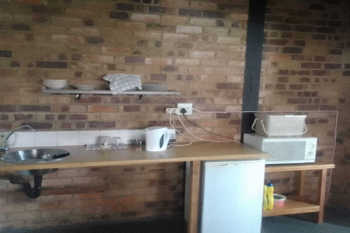 A basic kitchenette area featuring a stainless steel sink, exposed brick walls, and open shelving in an industrial-style setting.