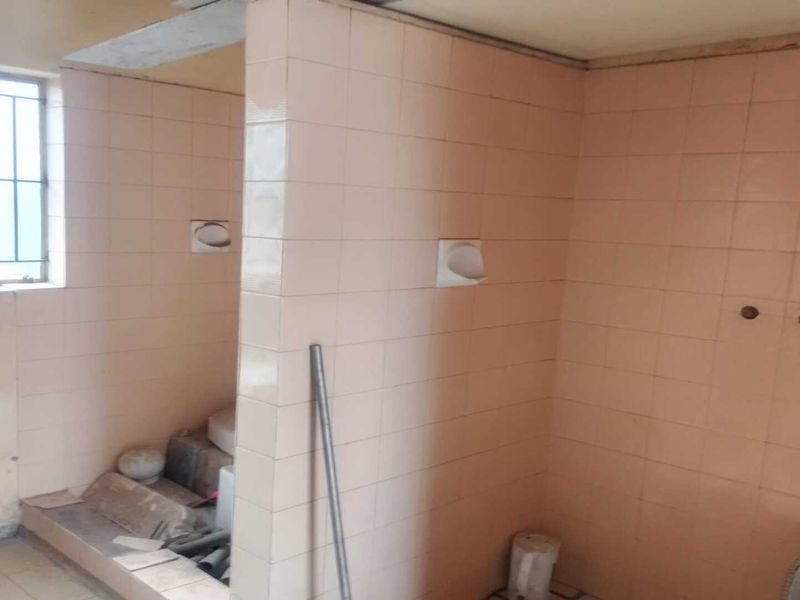 A dated industrial utility or wash area featuring tiled walls, security window bars, and exposed plumbing connections, requiring significant renovation and modernization.