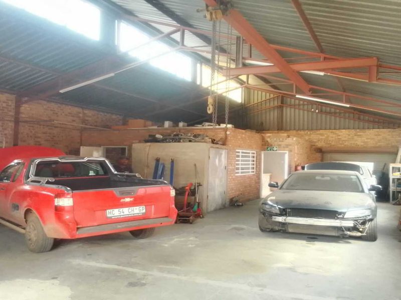 Spacious industrial workshop featuring high ceilings, exposed steel roof trusses, overhead crane, and concrete flooring, suitable for automotive or manufacturing operations.