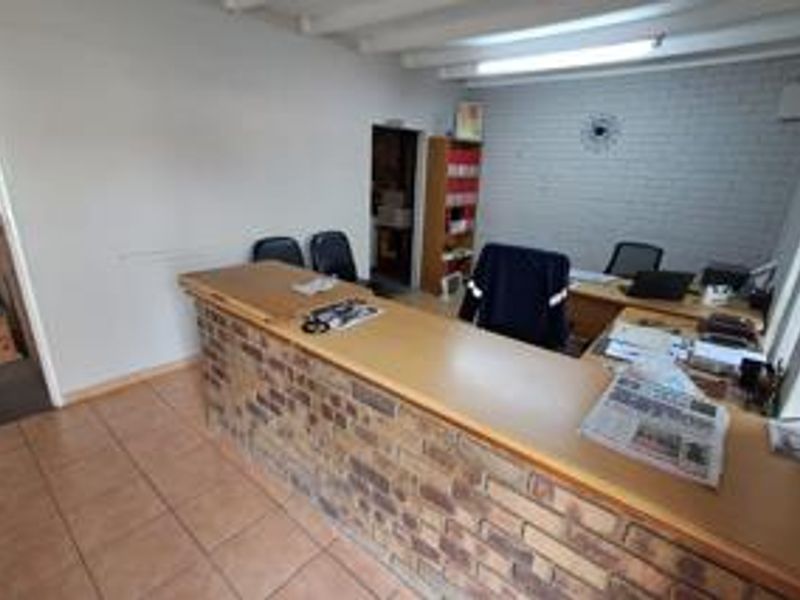 Functional industrial office space featuring a built-in brick reception counter, tiled flooring, and exposed beam ceiling.