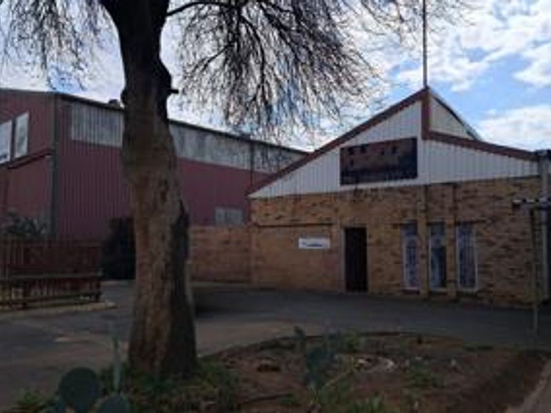 Exterior view of an industrial property featuring brick and metal cladding construction with an adjacent warehouse structure and paved yard area.