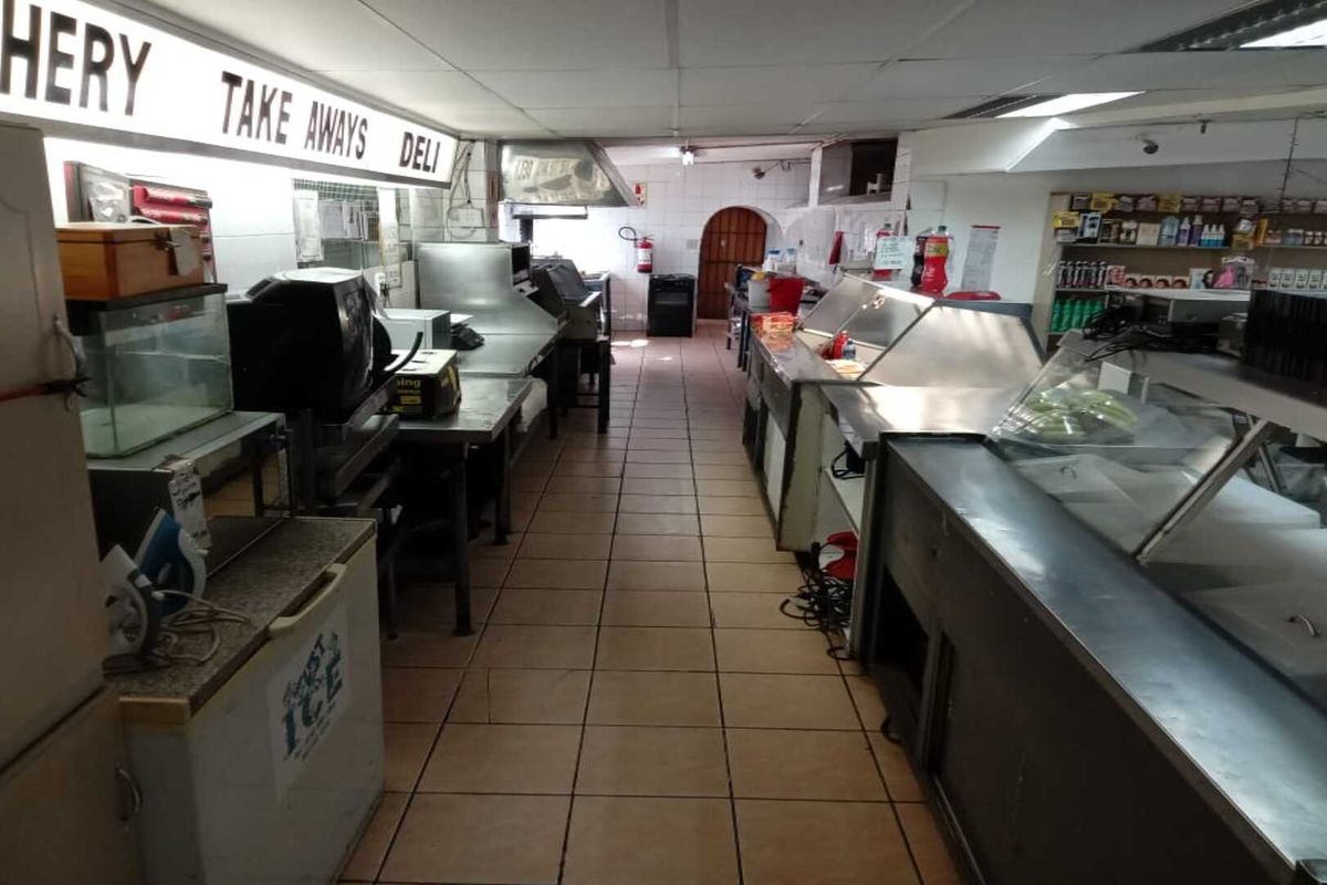 Commercial kitchen and deli area featuring stainless steel prep counters, display cabinets, and tiled flooring in a functional retail layout.