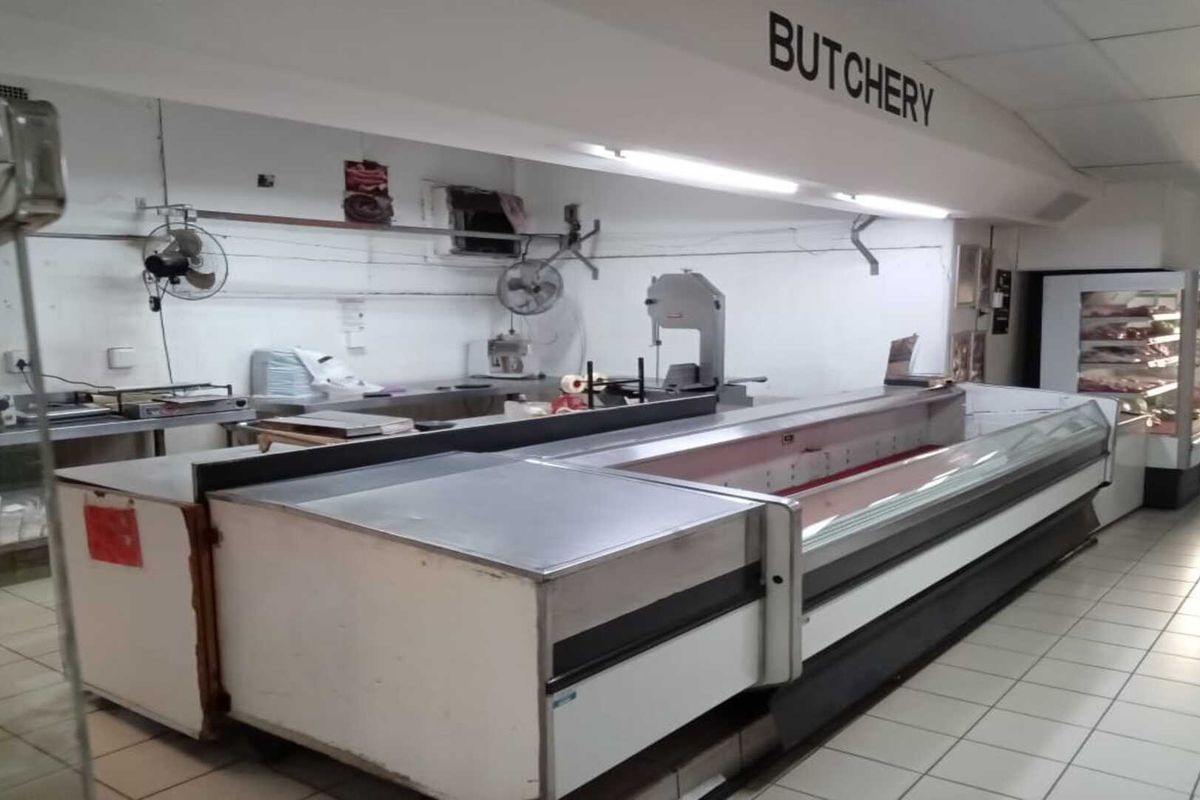 A commercial butchery section featuring built-in refrigerated display counters, stainless steel prep surfaces, and overhead lighting within a tiled retail environment.