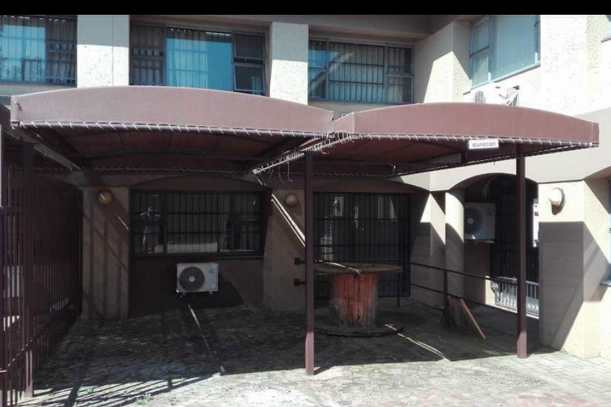 Exterior view of a business property featuring a covered parking or patio area with metal awnings and wall-mounted air conditioning units.
