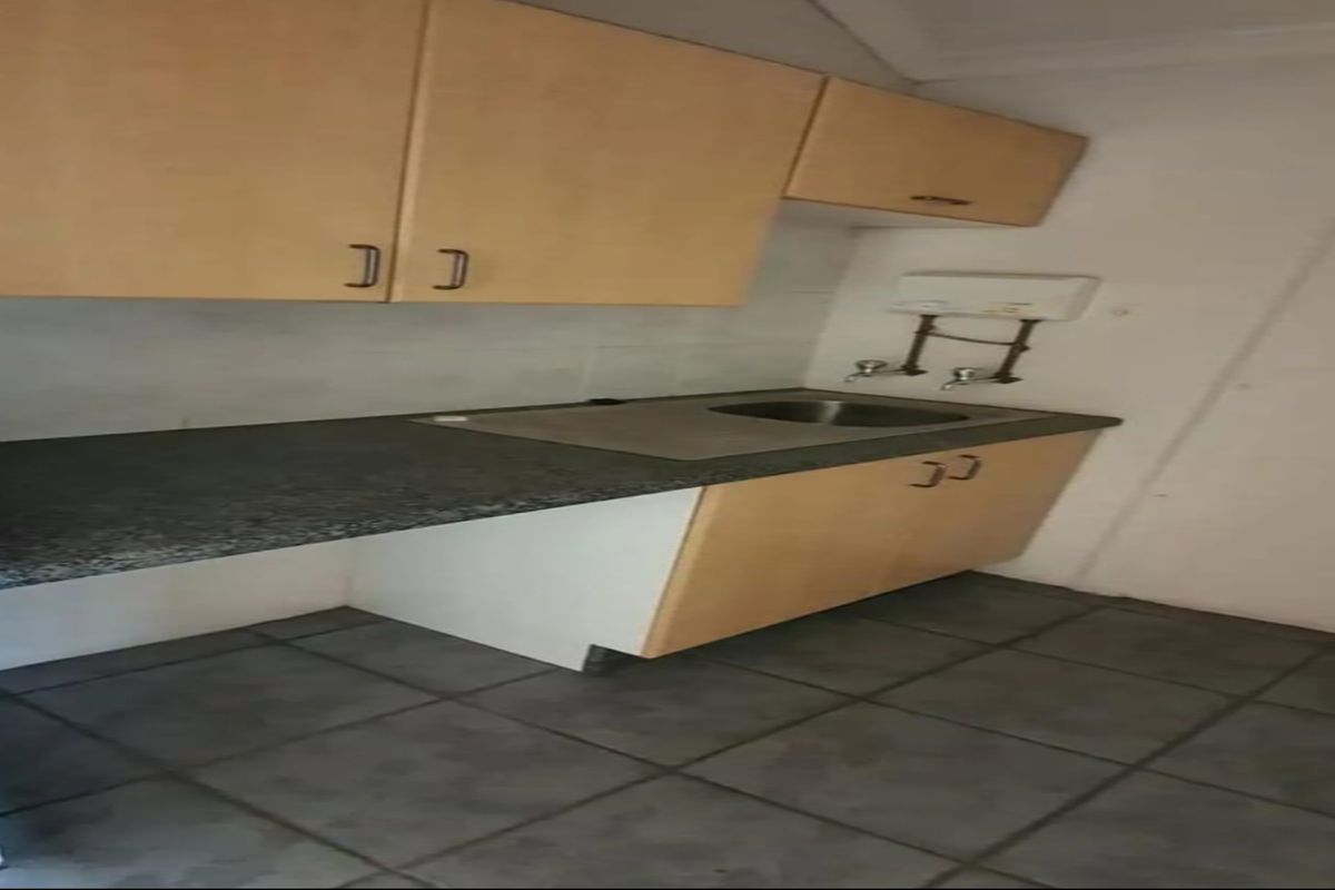 A compact kitchenette featuring laminate cabinetry, a dark stone-look countertop, a stainless steel sink, and tiled flooring.