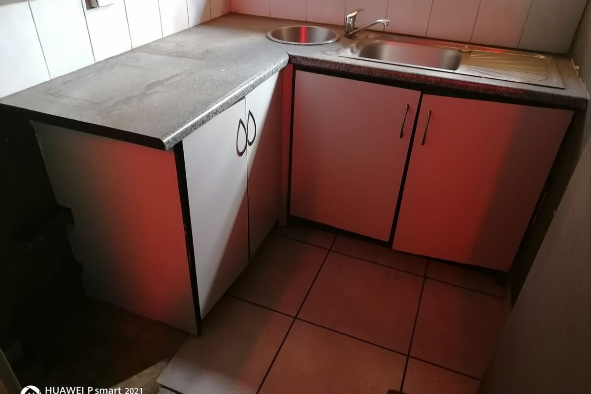 A compact kitchen area featuring built-in cabinetry, a stainless steel sink, and tiled flooring, suitable for a small utility or prep space.