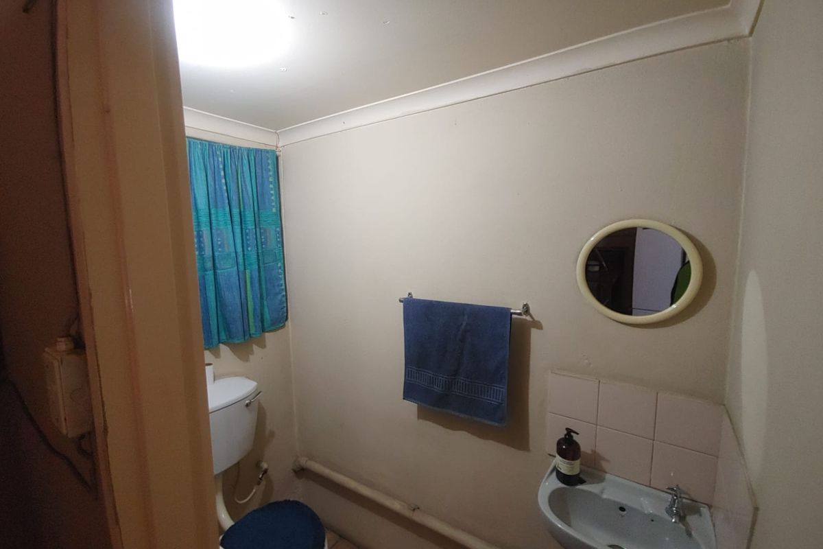 A compact industrial-style bathroom featuring a wall-mounted basin, standard toilet, and exposed plumbing fixtures.