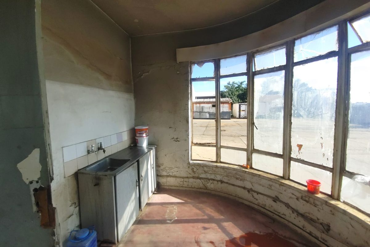 A dilapidated interior space featuring a small kitchenette area with a sink, large curved windows, and significant signs of structural wear and surface deterioration.