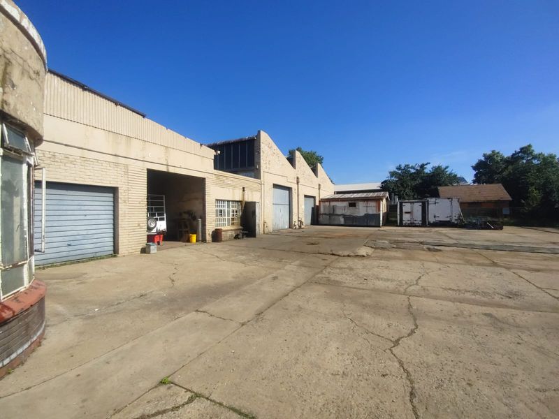Industrial property exterior featuring multiple roller shutter doors, a large concrete yard area, and functional warehouse access points.
