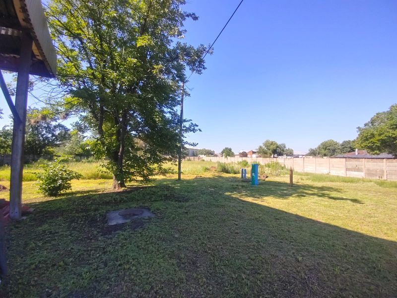 A spacious outdoor industrial yard area featuring a large tree, perimeter concrete walling, and open grass space.