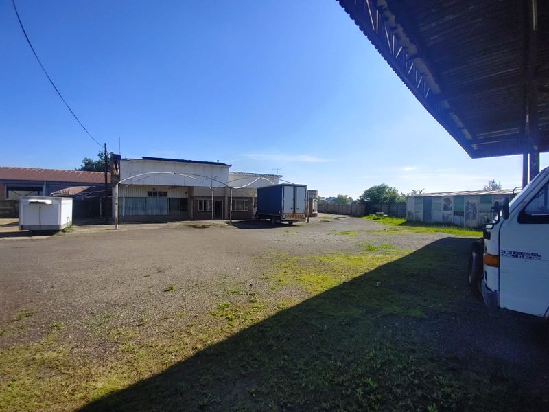 Industrial property exterior featuring a large gravel yard, covered loading area, and main building structure with visible signs of wear.