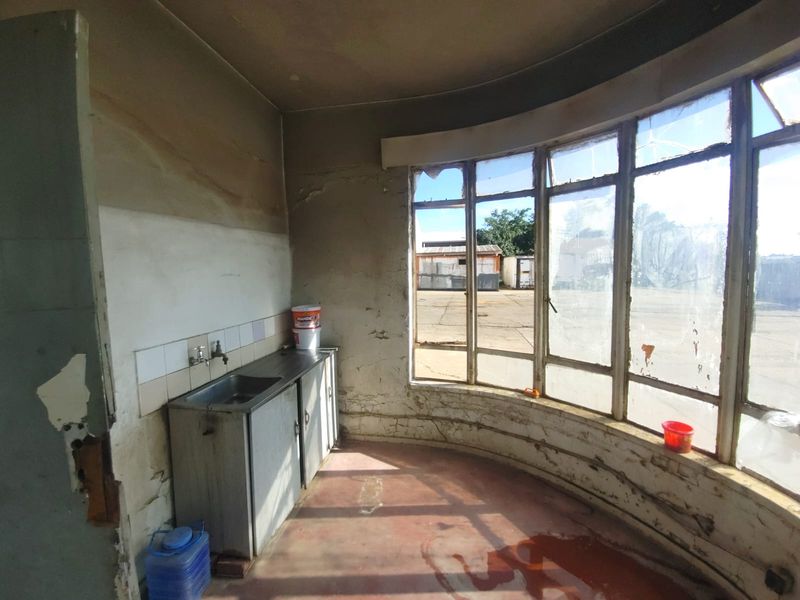 A dilapidated interior space featuring a small kitchenette area with a sink, large curved windows, and significant signs of structural wear and surface deterioration.