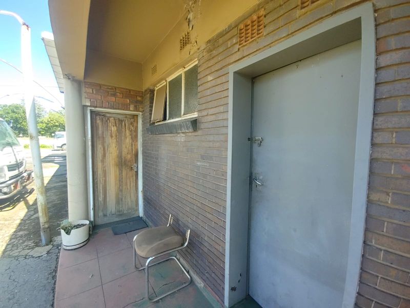 Exterior view of an industrial building entrance featuring brick facade, metal door, and a secondary wooden door with visible signs of wear.