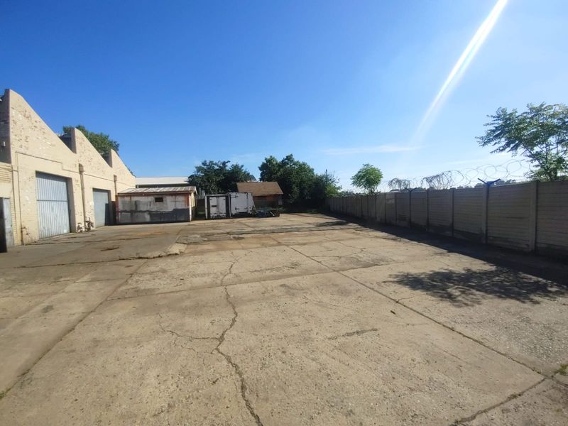 Spacious industrial yard featuring concrete paving, perimeter walling with security fencing, and access to industrial building structures.